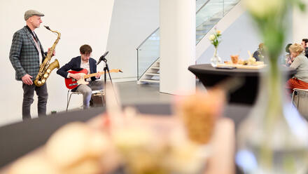 Ein Saxophonist und ein Gitarrist spielen in der Fundatie, w&auml;hrend die Leute zuh&ouml;ren.