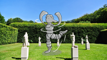 Es gibt mehrere Statuen im gr&uuml;nen Gras. Der Himmel ist blau. Eine gezeichnete Version von Mikkel tanzt zwischen den Statuen auf dem Bild.