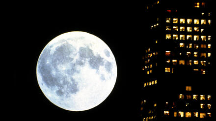 Filmstill aus &bdquo;Koyaanisqatsi&ldquo;, der einen Vollmond neben einem Wohnblock zeigt