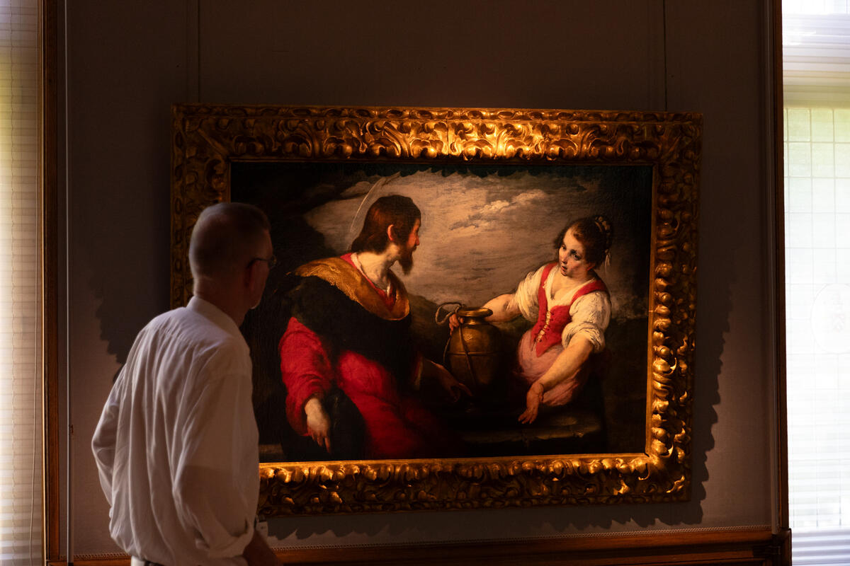 Een man staat voor een 17e eeuws schilderij van volwassen man en meisje in rode kleding. Het schilderij wordt mooi belicht door een spot en is omlijst met een goudkleurige lijst.