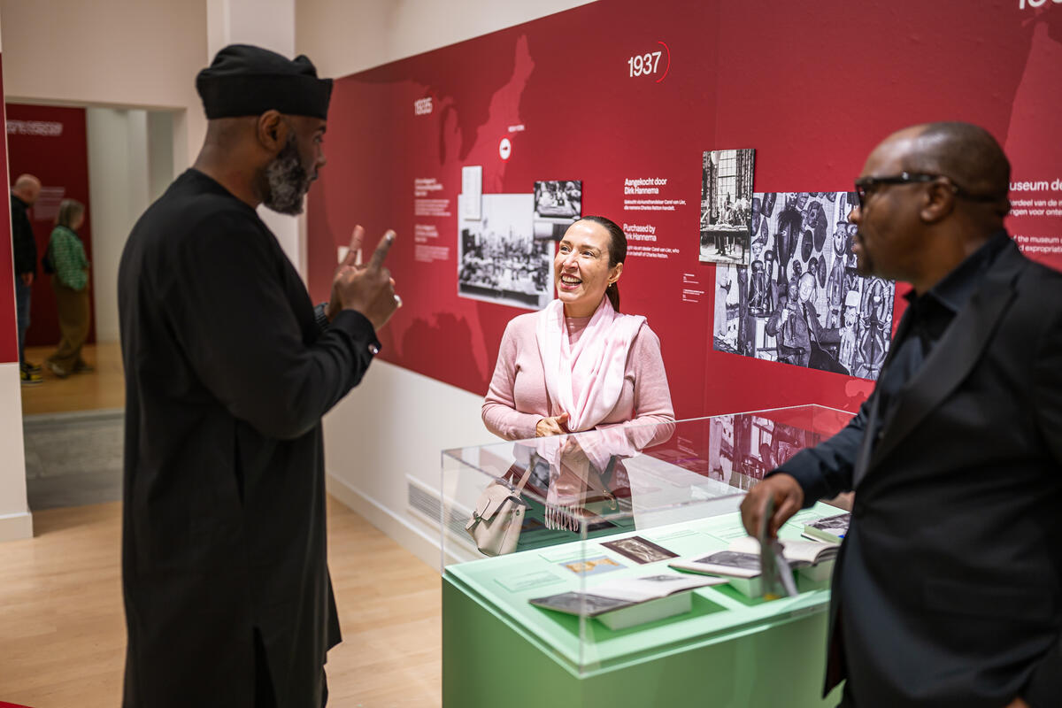 Twee Nigeriaanse mannen praten met een vrouw en lachen tijdens de opening van Back to Benin.
