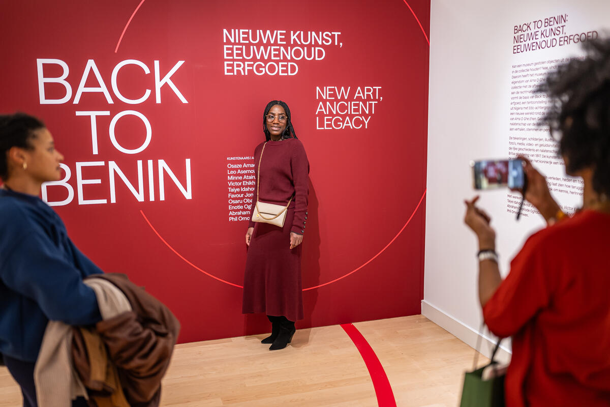 Een vrouw neemt een foto voor een rode muur waarop staat: Back to Benin