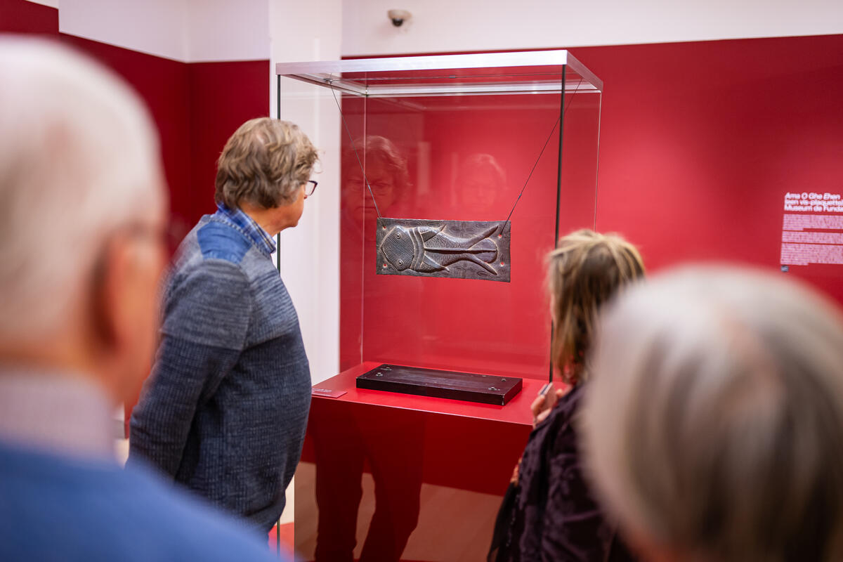 Mensen staan in een rode ruimte en kijken naar een bronzen plakaat van een moddervis.