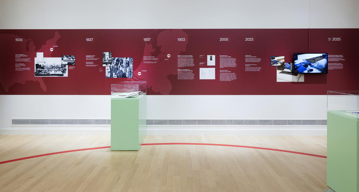 Een muur van het museum met daarop een rode strook op de muur. Op deze strook staat allemaal informatie en foto's van het herkomstonderzoek van Back to Benin.