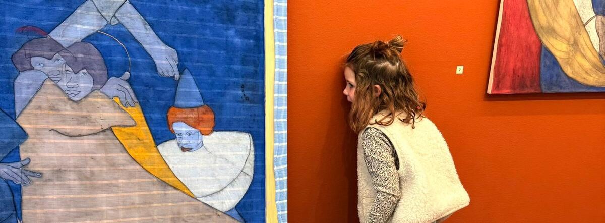 Een klein meisje staat met haar gezicht tegen een oranje muur. Ze kijkt naar de achterkant van een schilderij.