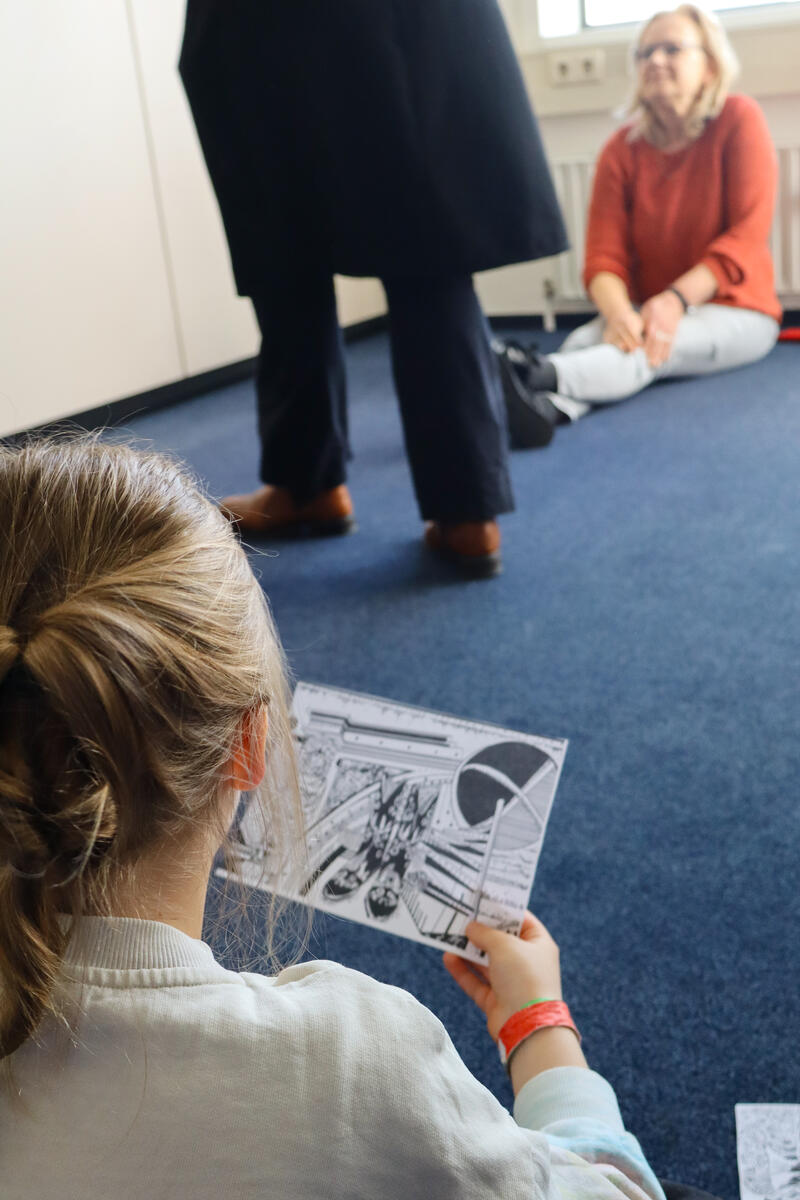 Een jong meisje heeft een tekening in haar handen en kijkt hiernaar. Alleen haar rug is zichtbaar.