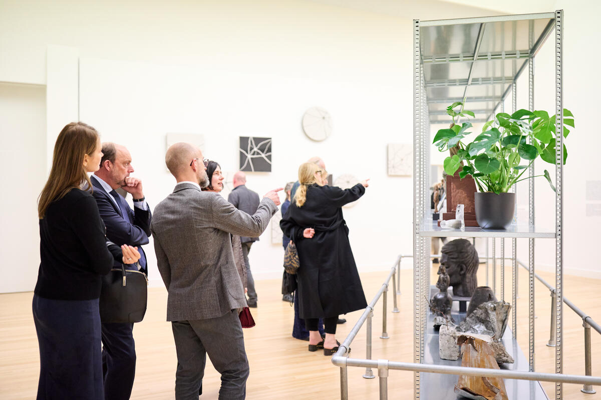 Mensen in pakken staan voor een kunstwerk en praten met elkaar.