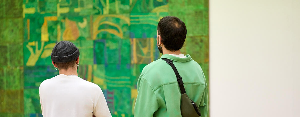 Twee mannelijke bezoekers staan voor een groot groen schilderij met gele accenten. Een van de mannen draagt zelf een groen shirt.
