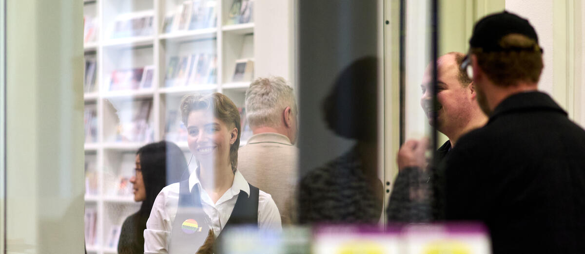 Medewerkers van de Fundatie lachen en praten met elkaar. Ze zijn gefotografeerd door een glazen deur heen.