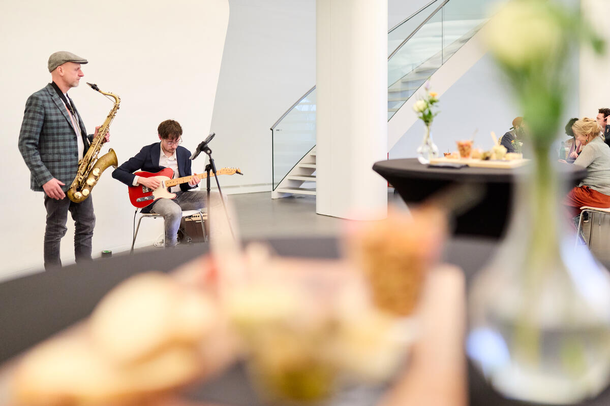 Een saxofonist en guitarist spelen in de Fundatie, terwijl mensen luisteren.