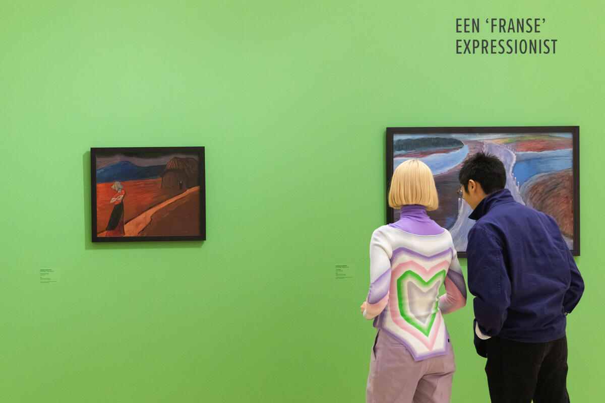Twee jonge bezoekers staan voor een knalgroene muur. Aan de muur hangen twee schilderijen.