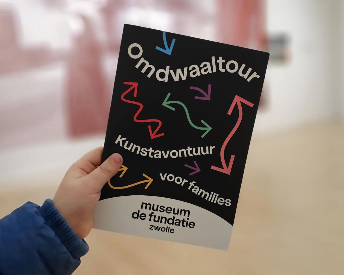 Een kind houdt de flyer vast van Omdwaaltour. Op de flyer staat: Kunstavontuur voor families.