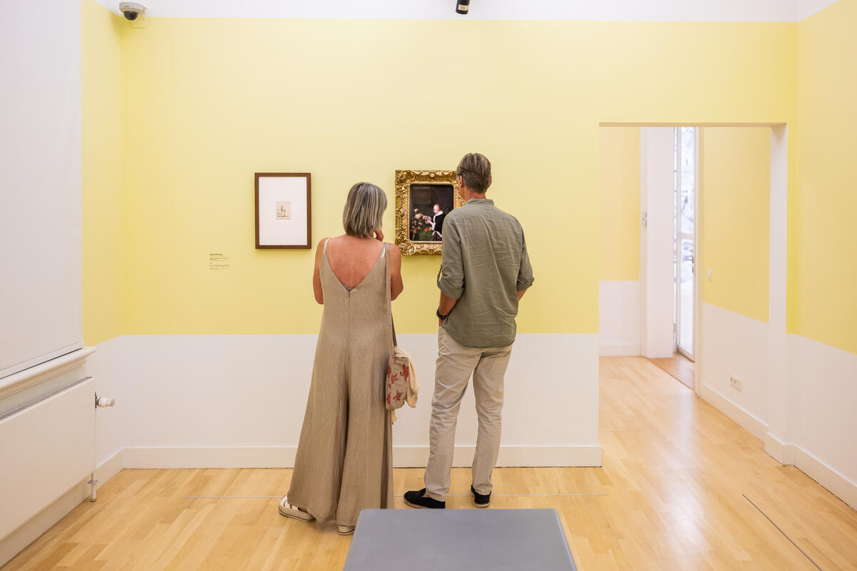 Twee bezoekers staan voor een lichtgele muur waar een klein schilderij van Ter Borch hangt. 