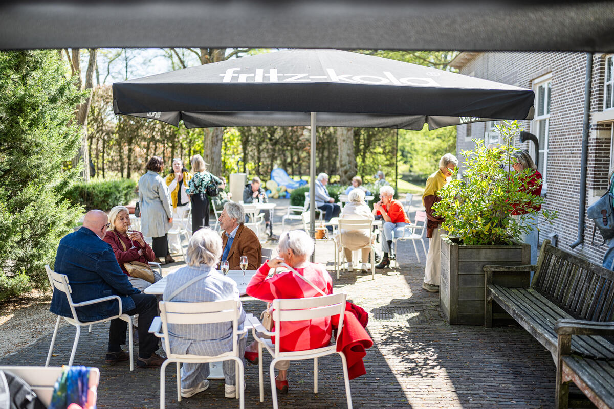 Mensen zitten op het terras buiten bij Kasteel het Nijenhuis, omringd met groene planten.