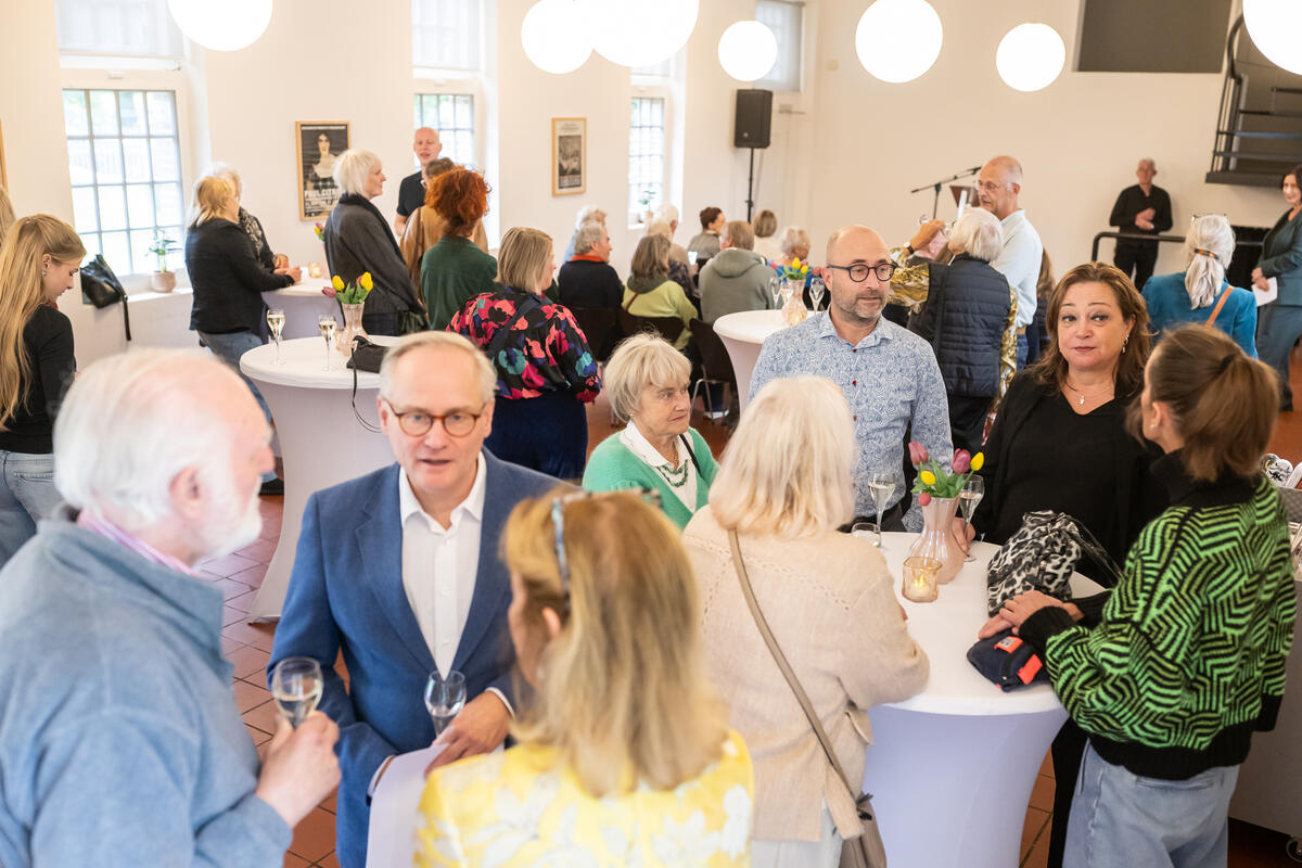 Mensen staan aan witte tafels te praten binnen Kasteel het Nijenhuis. Er is een evenement gaande.