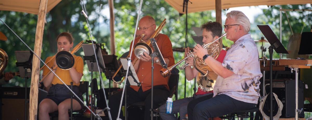Vier muzikanten met blaasinstrumenten spelen in de buitenlucht.