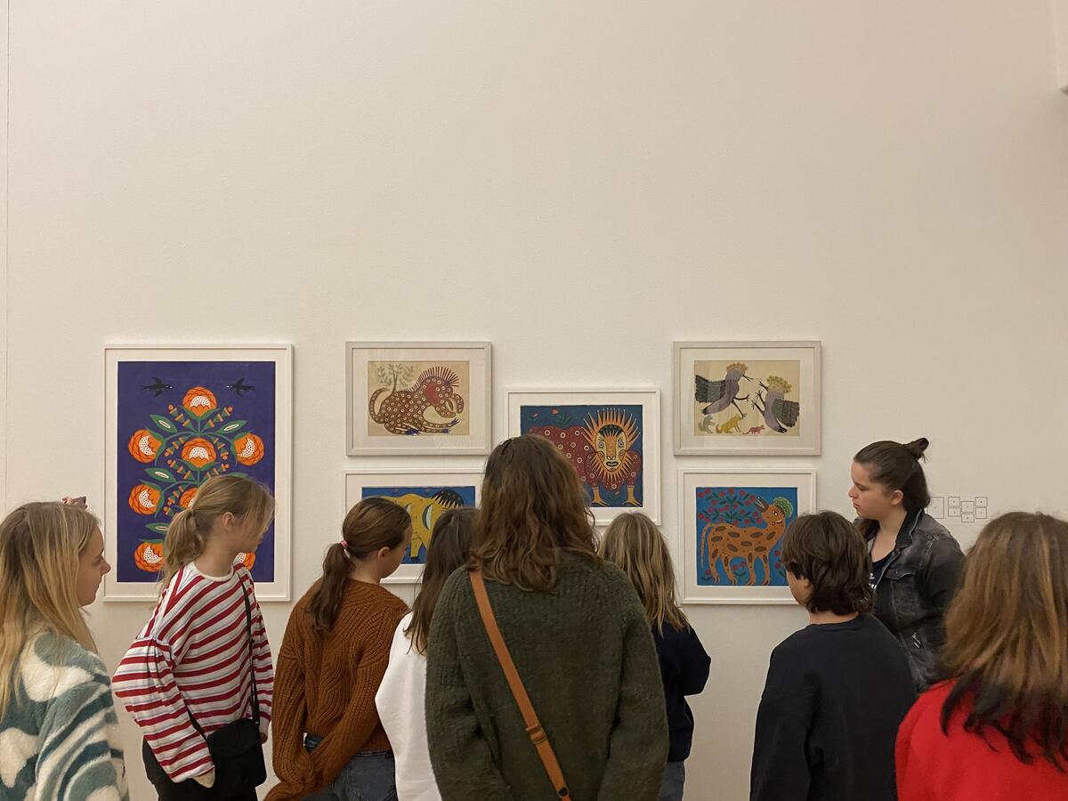 Een groep scholieren staan voor een muur vol verschillende schilderijen. 