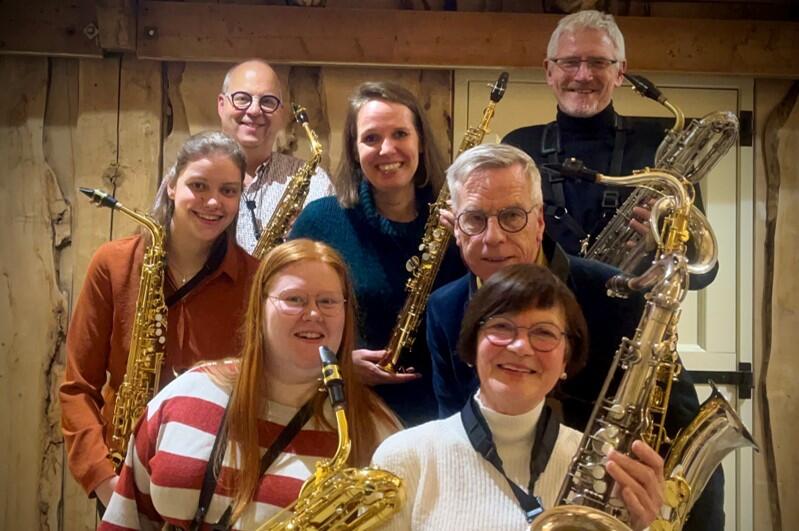 Zes saxofonisten staan lachend op de foto met hun saxofoon.