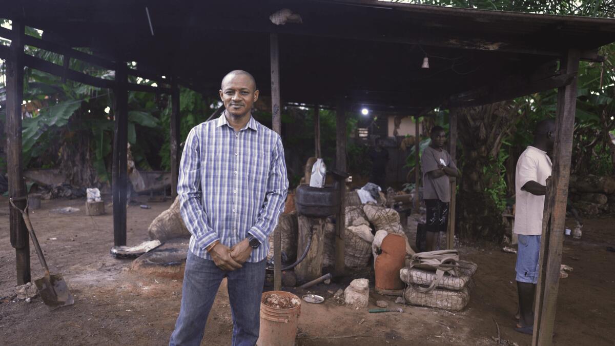 Een Nigeriaanse man, Phil Omodamwen staat voor een houten overkapping.