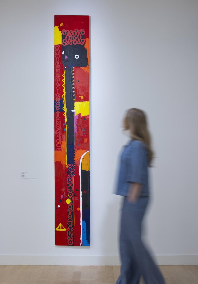 Verticaal hoog schilderwerk van Marcel Pinas, met iemand die er langs loopt