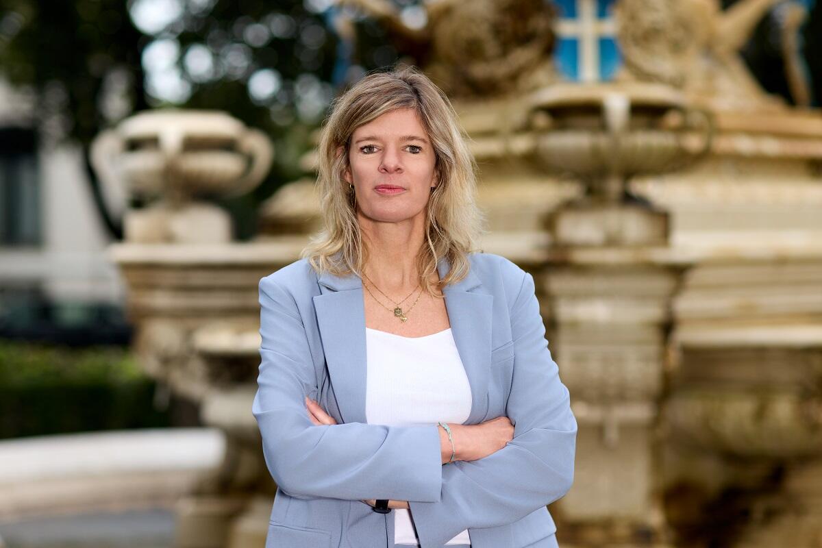 Portretfoto van Rinette van der Vliet. Ze staat met haar armen over elkaar heen geslagen en met een glimlach op de foto.