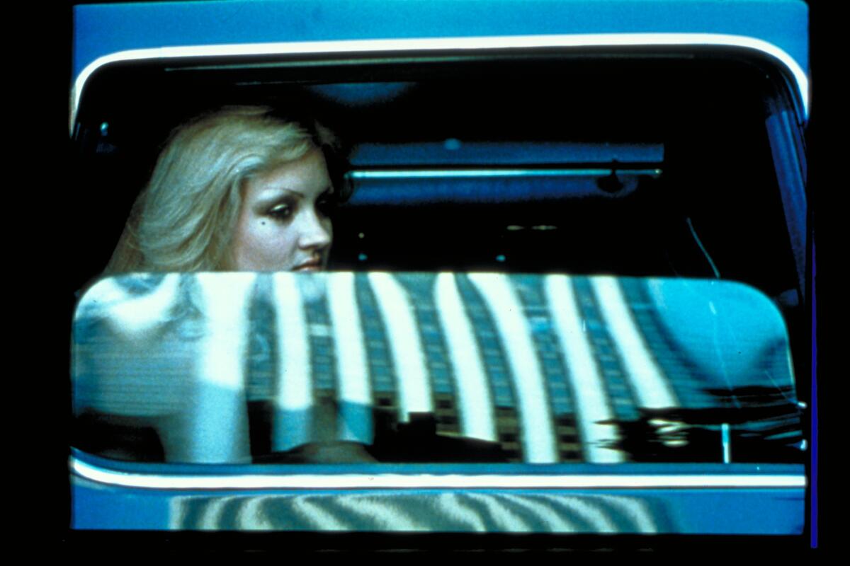Ein Standbild aus &bdquo;Koyaanisqatsi&ldquo;, das eine Frau als Beifahrerin in einem Auto mit halb ge&ouml;ffnetem Fenster zeigt