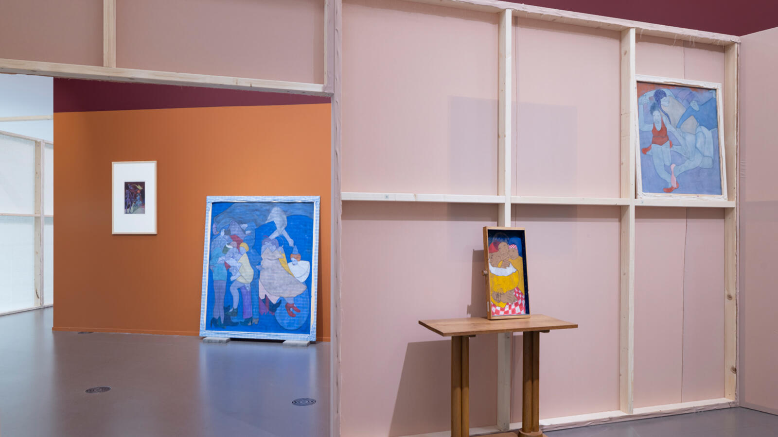 Schilderijen hangen op gekleurde muren in oranje en roze tinten. 