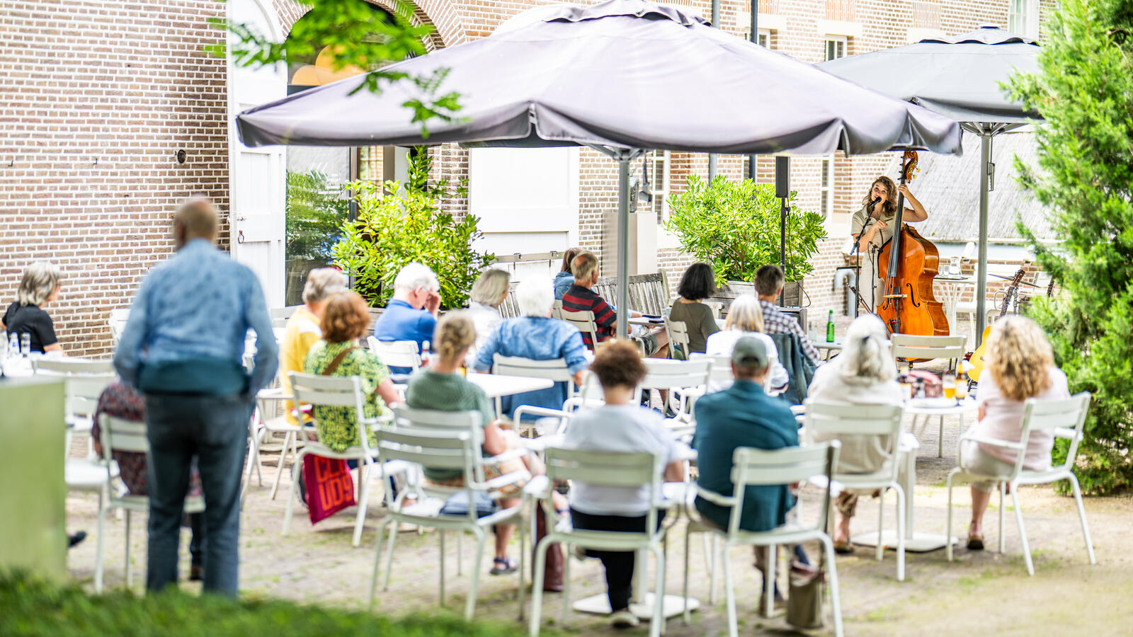 Het terras van Kasteel het Nijenhuis. Mensen zitten op witte stoelen buiten onder parasols.