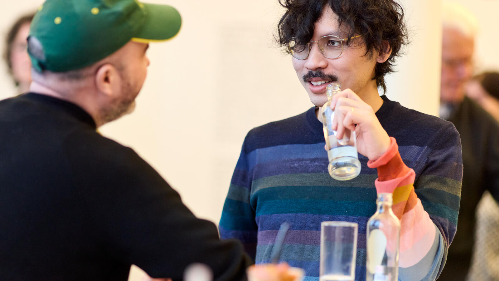 Twee jonge bezoekers kletsen en drinken een drankje. Een van hen draagt een groene pet.