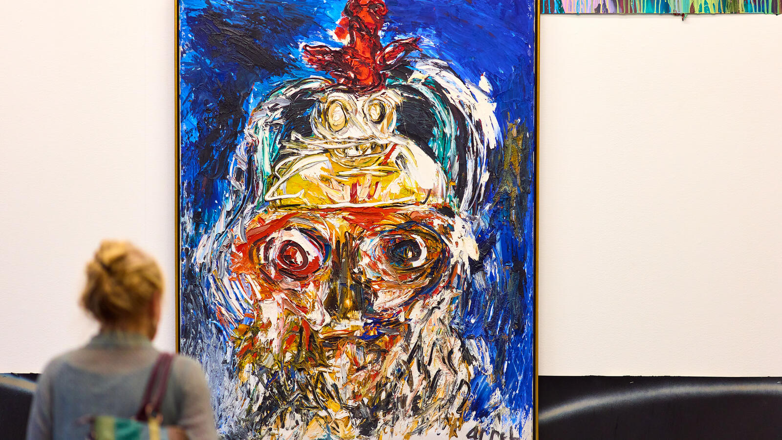 Een vrouw kijkt naar een groot kleurrijk schilderij van Karel Appel.