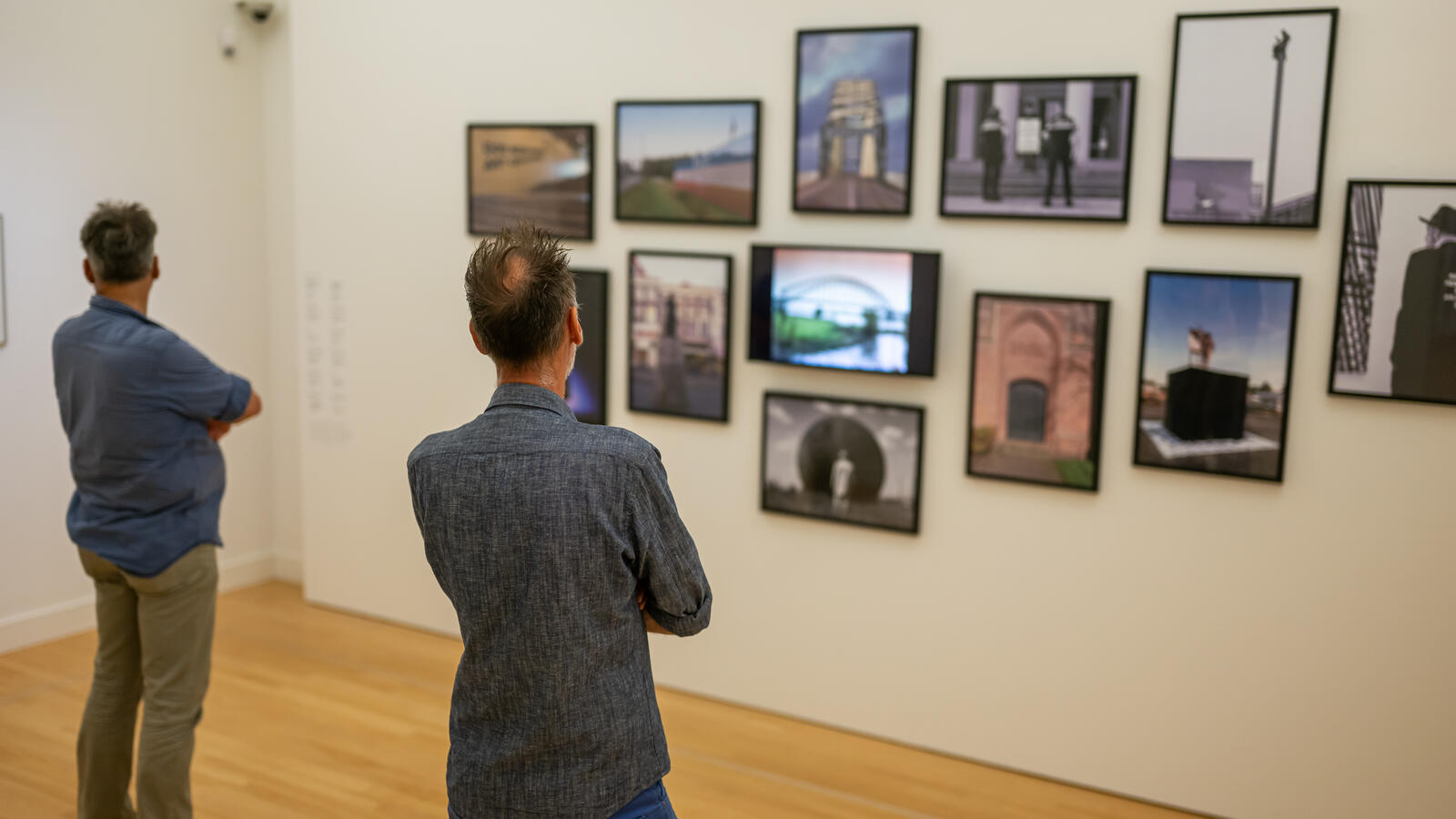 Twee bezoekers kijken naar een muur waar verschillende foto's hangen.