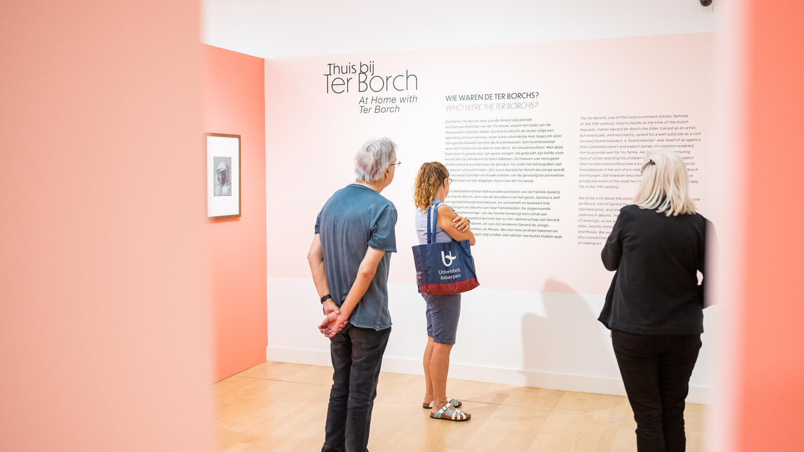 Drie bezoekers lezen de tekst op de muur bij de tentoonstelling over Ter Borch. De muren zijn roze.