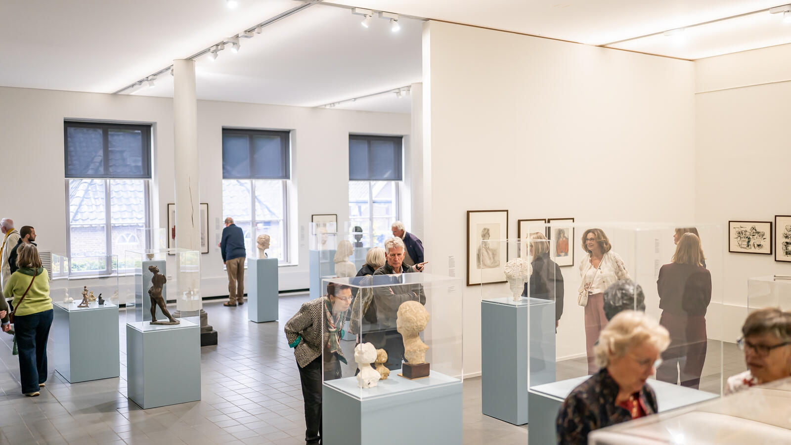 Een wijde foto van de zaal met daarin allerlei lichtblauwe sokkels met beelden en bezoekers die rondlopen.
