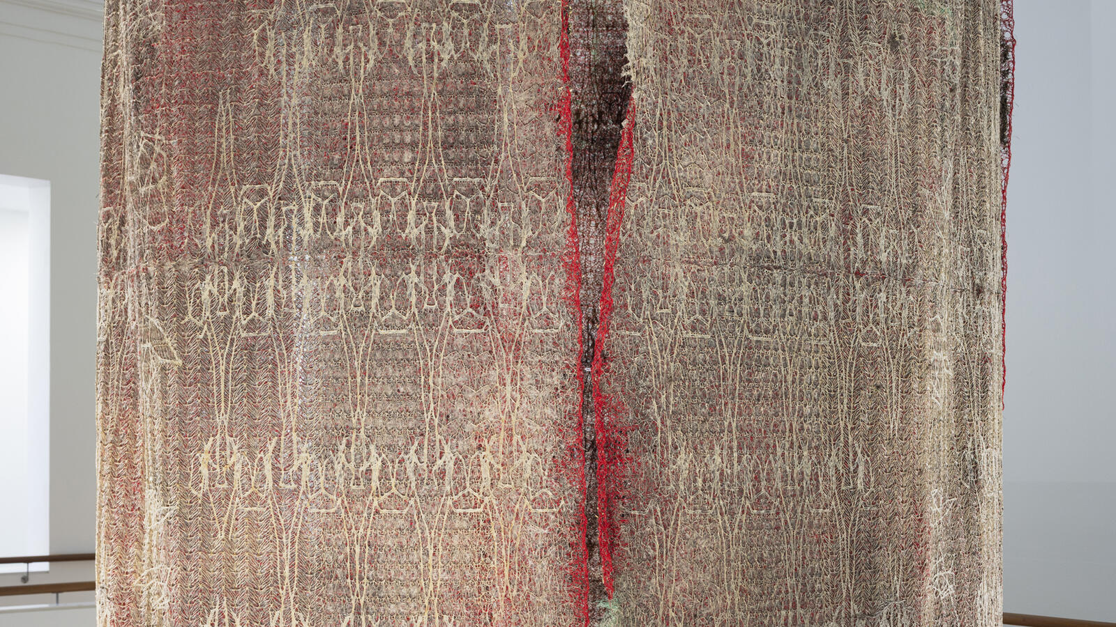 groot hangend kunstwerk van gedroogde plantenwortels en rode stof van Diana Scherer gefotografeerd als close-up waardoor het patroon goed zichtbaar is.