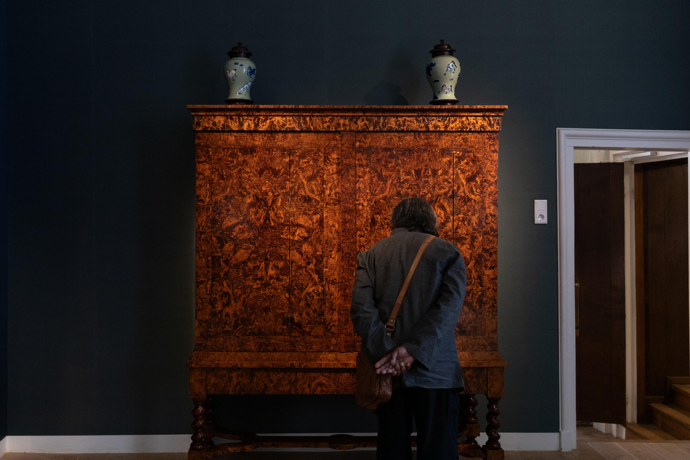 Een bezoeker staat voor een statische houten kast. De muur en de kleding van de bezoeker zijn donker. Daardoor lijkt de kast haast licht te geven.