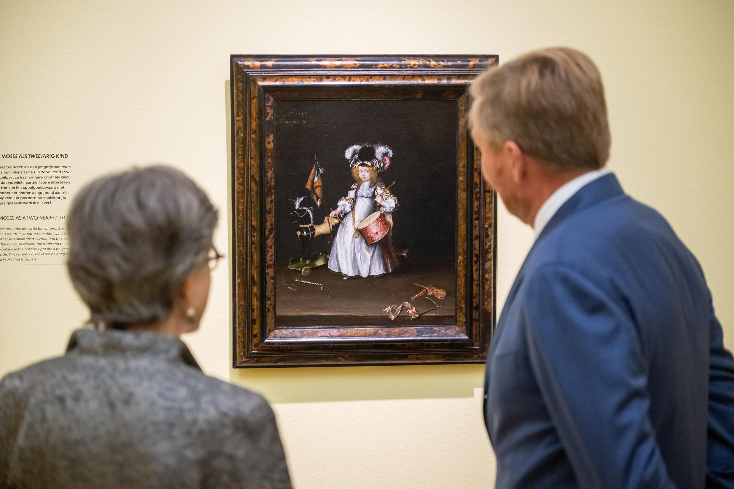 Koning Willem-Alexander staat met een vrouw voor een van de bekende werken van Gesina ter Borch, Portret van Moses ter Borch als tweejarig kind. Op het schilderij is broertje Moses te zien in een jurk met wit schort en eenhoed met veren die scherp afsteken tegen de donkere achtergrond. De jongen draagt een trom en trommelstokken.