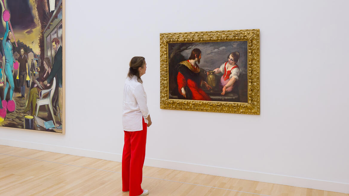 Een bezoeker staat in een zaal en kijkt naar het schilderij van Christus en de Samaritaanse Vrouw bij de Bron.
