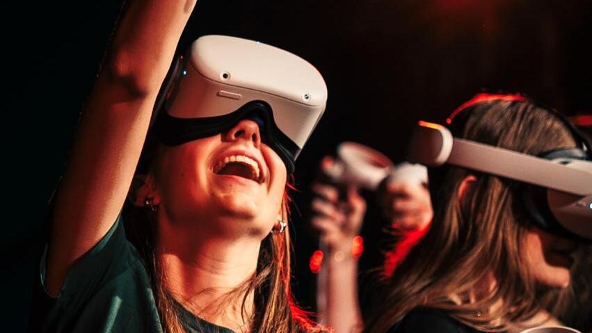 iemand met een vr bril en haar arm omhoog met een afstandsbediening in haar hand