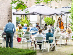 Het terras van Kasteel het Nijenhuis. Mensen zitten op witte stoelen buiten onder parasols.
