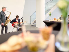 Een saxofonist en guitarist spelen in de Fundatie, terwijl mensen luisteren.