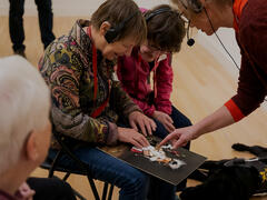 Two people with visual impairments are running their hands over a tactile painting. A museum guide is standing nearby, explaining things.