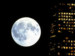 A still from *Koyaanisqatsi* showing a full moon next to a block of flats